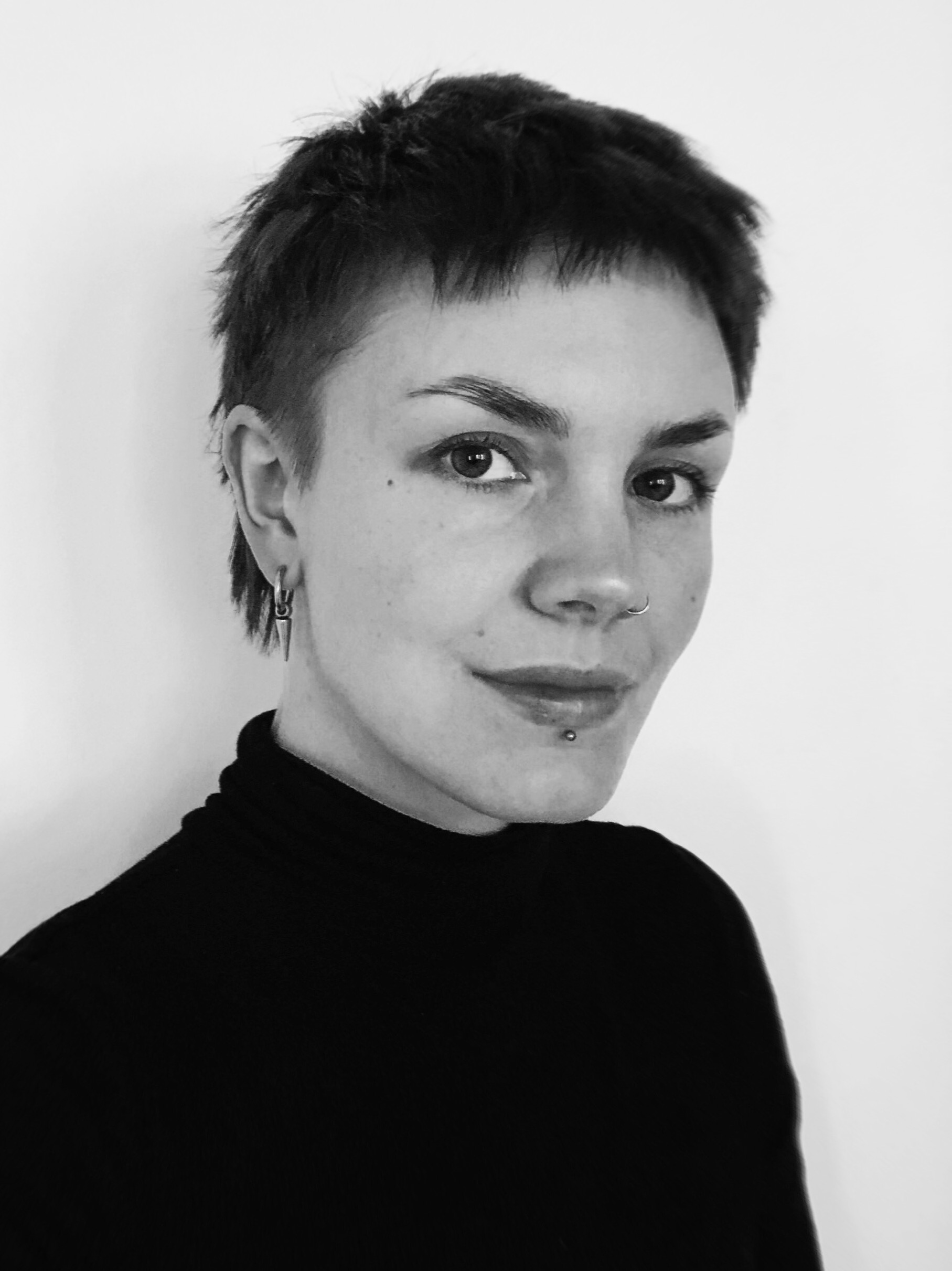 Black and white profile photo of me looking at the camera. I am a white woman in her 30s with a short haircut wearing a black turtleneck.